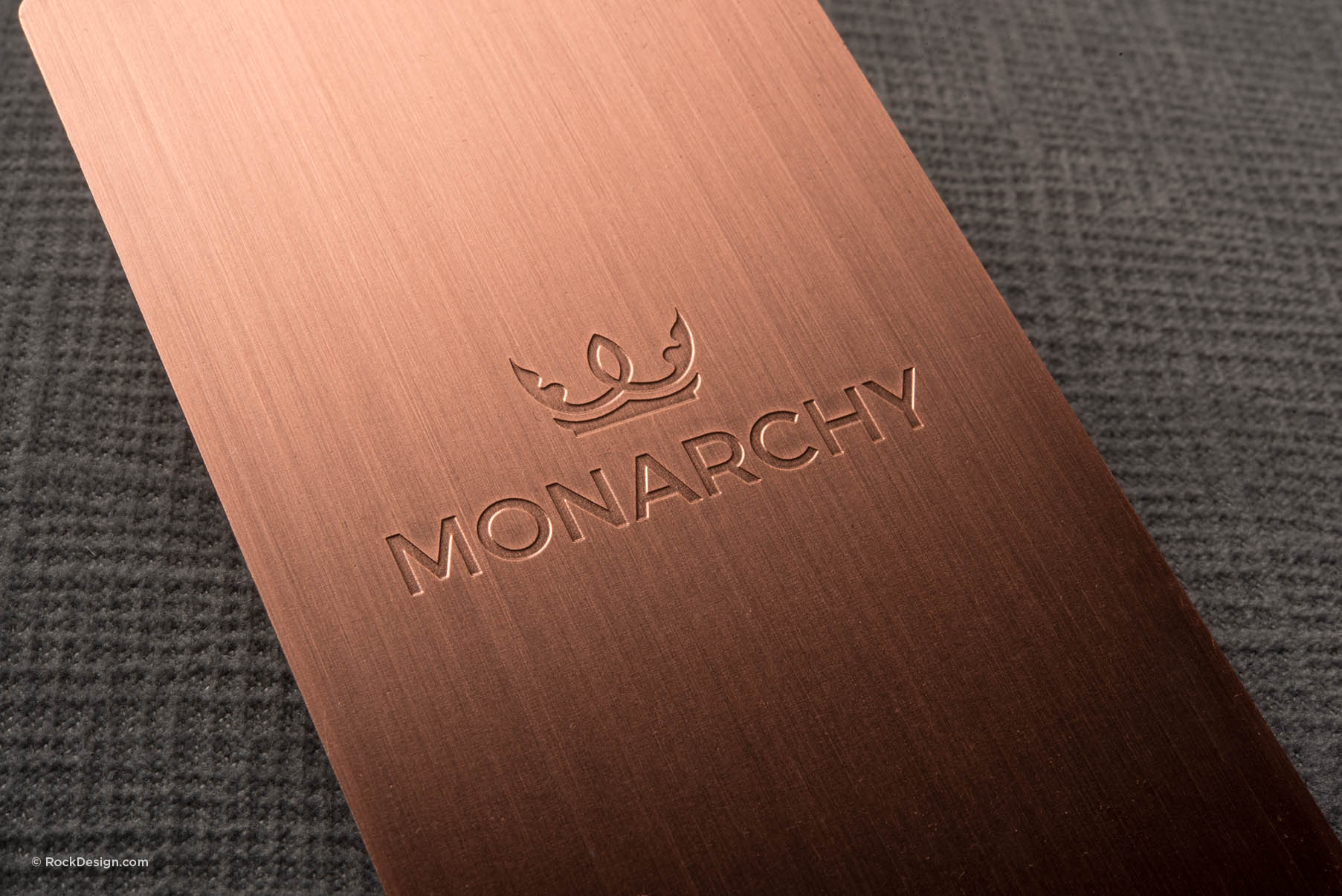 Sleek copper metal business card featuring etched Monarchy crown logo on brushed metallic finish.