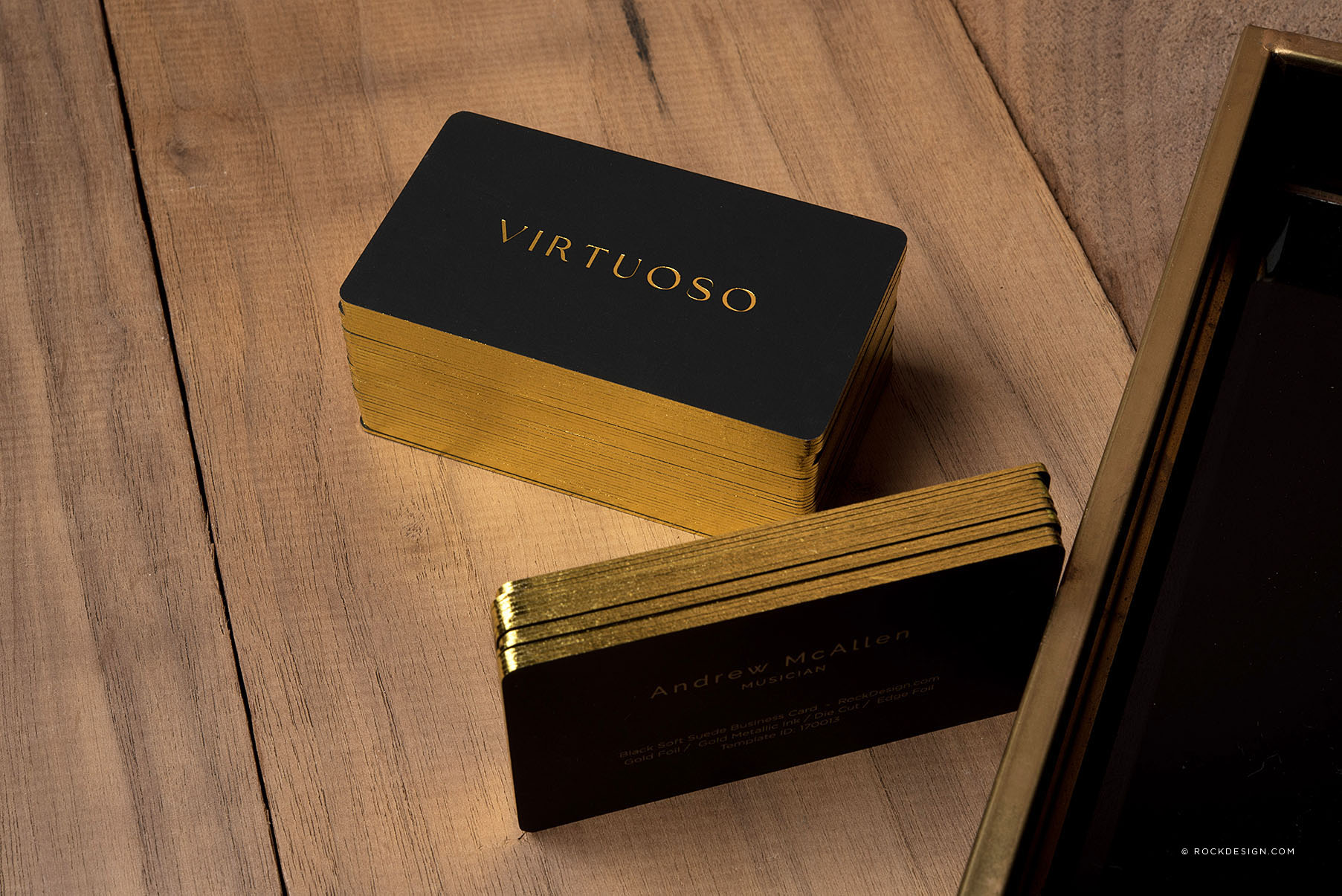 Black soft suede business cards with gilded gold foil edges and gold metallic text on a wooden surface.